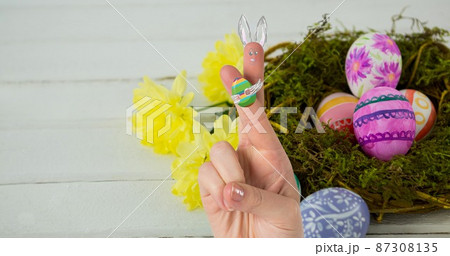 Cropped hand with creative bunny cartoon drawing on crossed fingers over easter eggs in nest 87308135