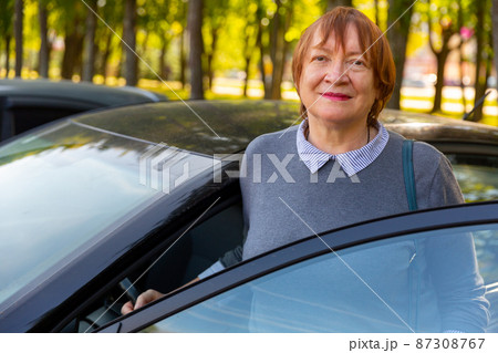 Positive mature woman standing beside her car 87308767