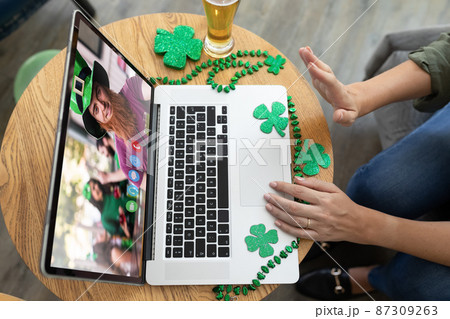 Caucasian woman at bar making st patrick's day video call waving to friend in costume on laptop Caucasian woman at bar making st patrick's day video call waving to friend in costume on laptop 87309263