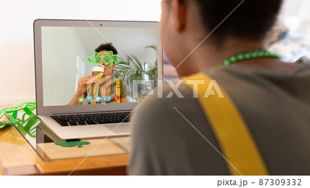 Mixed race woman having st patrick's day video call with friend drinking beer on laptop at home Mixed race woman having st patrick's day video call with friend drinking beer on laptop at home 87309332