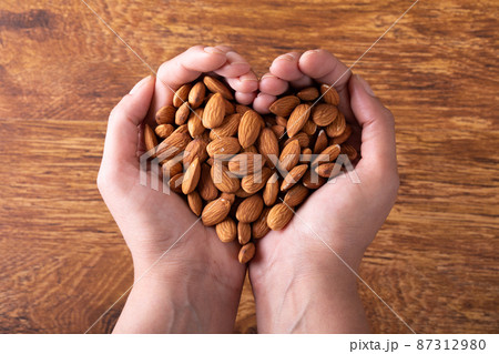 Cropped hands holding nutritious almonds in heart shape on wooden table 87312980