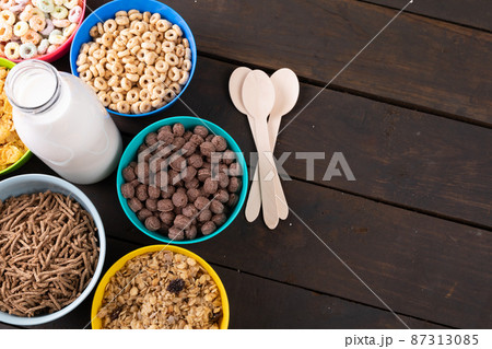 Various breakfast cereals in bowls around milk bottle on wooden table 87313085