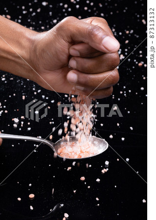 Cropped hand of african american man sprinkling himalayan salt on spoon against black background Cropped hand of african american man sprinkling himalayan salt on spoon against black background 87313132