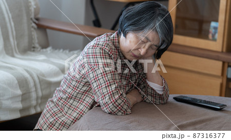 疲れてこたつで頬杖をついて寝ている80代のシニア女性 87316377