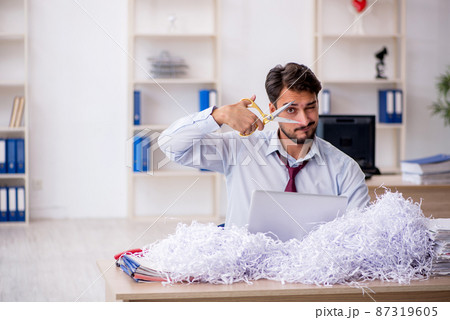 Young male employee and a lot of cut papers in the office Young male employee and a lot of cut papers in the office 87319605