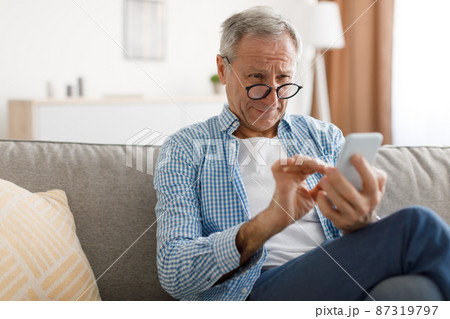 Mature man squinting using mobile phone, looking at screen 87319797