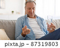 Mature man taking pills holding glass of water 87319803