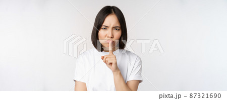 Angry asian girl shushing, keep quiet, taboo silence gesture, press finger to lips and frowning, scolding for being too loud, standing over white background Angry asian girl shushing, keep quiet, taboo silence gesture, press finger to lips and frowning, scolding for being too loud, standing over white background 87321690