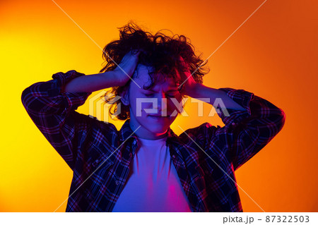 Portrait of young curly man in checkered shirt touching head in headache isolated over gradient yellow orange background in neon light 87322503