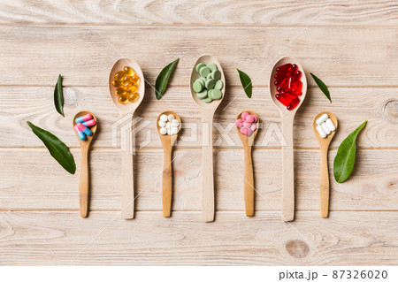 Top view Variety of vitamin and mineral pills in wooden spoon on Colored background. Top view of assorted pharmaceutical medicine pills. Dietary supplement healthcare product 87326020