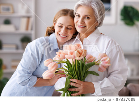 Delighted young woman congratulations mother with bouquet of fresh tulips Delighted young woman congratulations mother with bouquet of fresh tulips 87327089