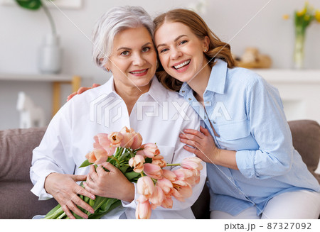 Delighted young woman congratulations mother with bouquet of fresh tulips Delighted young woman congratulations mother with bouquet of fresh tulips 87327092