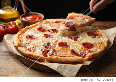 Woman taking slice of tasty pepperoni pizza at wooden table, closeup Woman taking slice of tasty pepperoni pizza at wooden table, closeup 87327644