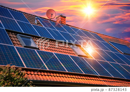 Photo collage of solar panels, photovoltaics on the red roof of a house and a beautiful sky with the setting sun. Alternative electricity source. Concept of sustainable resources 87328143