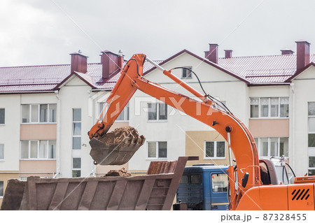 Excavation works. The bucket of the tractor loads the soil with a shovel into the back of a dump truck on the construction site Excavation works. The bucket of the tractor loads the soil with a shovel into the back of a dump truck on the construction site 87328455