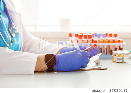 Hands of a doctor holding blood sample and making notes Hands of a doctor holding blood sample and making notes 87330111