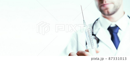 Syringe needle medical injection. Selective focus, doctor hand in blue gloves holding syringe with needle. Hospital white doctor gown, stethoscope. Syringe with flu vaccine with copy space. 87331013