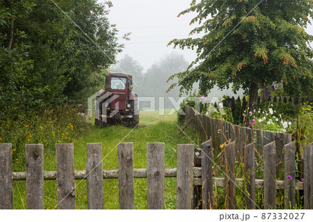 Agricultural tractor near trees and a wooden fence 87332027