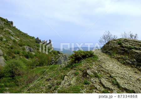 Horizontal background with a magnificent landscape of the Crimean Peninsula. Top view of the mountains covered with lush greenery and the thick clouds below the peaks. Clear blue sky. Copy space. 87334868