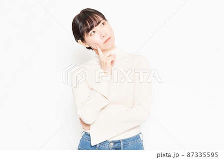 白背景の前に立って悩んでいるカジュアルな服装の女性 白背景の前に立って悩んでいるカジュアルな服装の女性 87335595