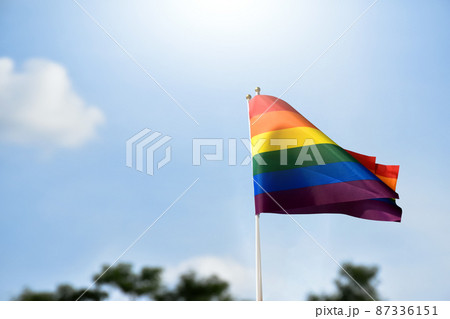 Rainbow flag, a symbol for the LGBT community, waving in the wind with a cloudy bluesky background.  87336151