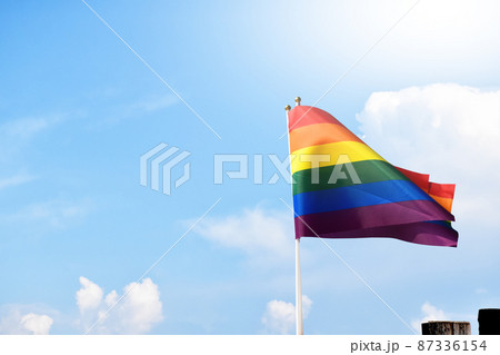 Rainbow flag, a symbol for the LGBT community, waving in the wind with a cloudy bluesky background.  87336154