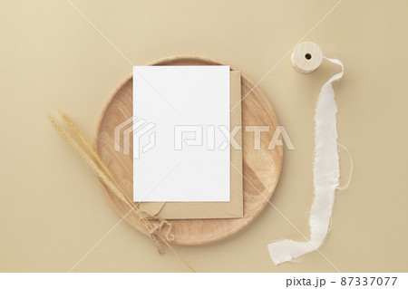 Blank greeting card invitation Mockup on Brown envelope with Dried bunny tails grass on beige background, Minimal table workplace composition, flat lay, mockup 87337077