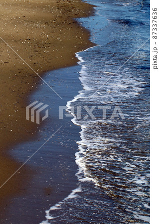 暖かい冬の午後の日差しをうける茶色い砂浜の静かな波打ち際の写真。 暖かい冬の午後の日差しをうける茶色い砂浜の静かな波打ち際の写真。 87337636