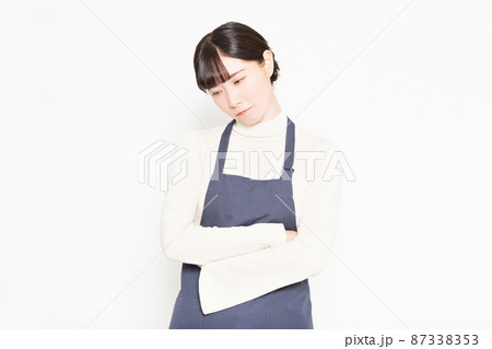 白い背景の前に立って悩んでいるエプロンをつけた女性 白い背景の前に立って悩んでいるエプロンをつけた女性 87338353