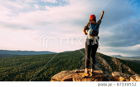 A traveler with a backpack in the mountains at sunset. A traveler with a backpack on the background of mountains, rear view. Hiking trips. A tourist girl on the background of a mountain landscape 87339552