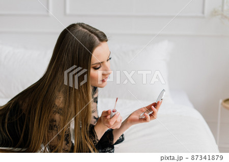 Beautiful lady doing her make up and hair in bedroom. Attractive young female with pretty long hair 87341879