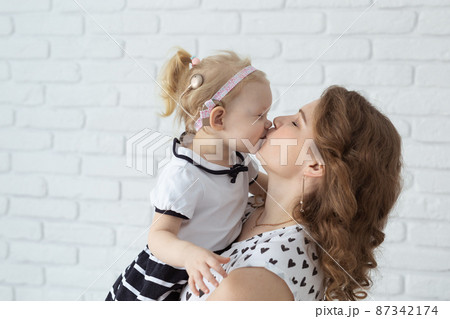 Mother holds her child with hearing aids and cochlear implants on white brick wall . Deaf and health concept 87342174