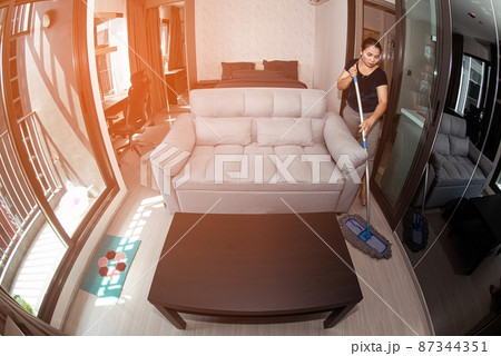 An Asian housewife is cleaning the floor with a broom in a room in the house. 87344351