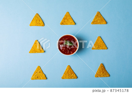 Overhead view of red sauce with rosemary amidst nacho chips arranged on blue background 87345178