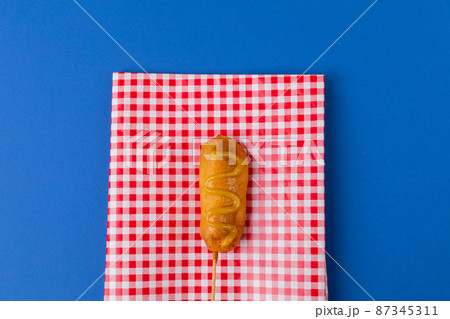 Directly above shot of corn dog with mustard sauce on checked pattern napkin over blue background Directly above shot of corn dog with mustard sauce on checked pattern napkin over blue background 87345311