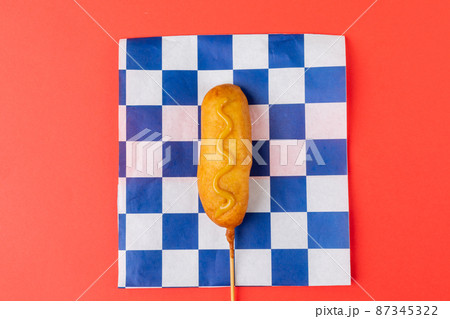 Directly above shot of corn dog with mustard sauce on checked pattern paper over red background 87345322
