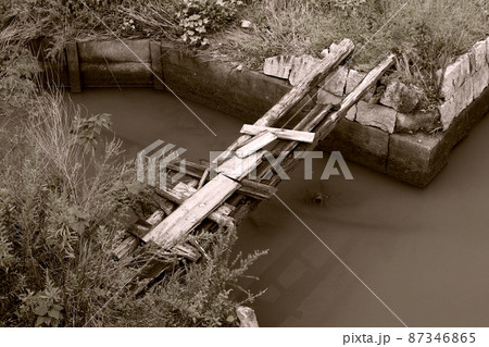 田園地帯の水路に設けられた崩れそうな木製橋の写真をレトロなモノトーンなセピア写真に画像加工。 87346865