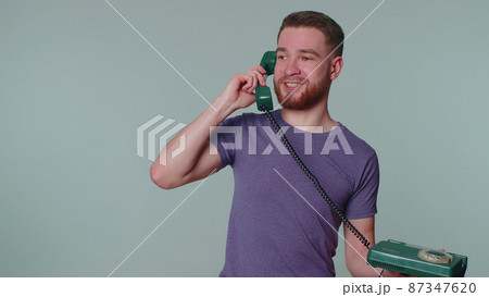 Cheerful tourist man secretary talking on wired vintage telephone of 80s, says hey you call me back Cheerful tourist man secretary talking on wired vintage telephone of 80s, says hey you call me back 87347620