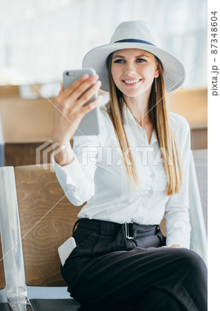 Woman talking on the phone at the airport terminal. Portarit of a young female traveler with a luggage and coffee cup and phone at the public transport stop on a sunny summer day Woman talking on the phone at the airport terminal. Portarit of a young female traveler with a luggage and coffee cup and phone at the public transport stop on a sunny summer day 87348604