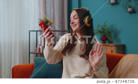Overjoyed young woman in wireless headphones dancing, singing on cozy couch in living room at home Overjoyed young woman in wireless headphones dancing, singing on cozy couch in living room at home 87348726