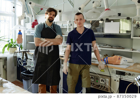 Two young specialists in workwear standing in large workshop Two young specialists in workwear standing in large workshop 87350029