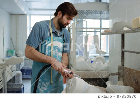 Side view of bearded skilled worker od prosthetic factory with electric cutter Side view of bearded skilled worker od prosthetic factory with electric cutter 87350870