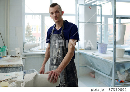 Contemporary young man in apron looking at camera during working process 87350892