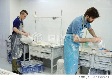 Two young male workers of prosthetic factory standing by tables Two young male workers of prosthetic factory standing by tables 87350923