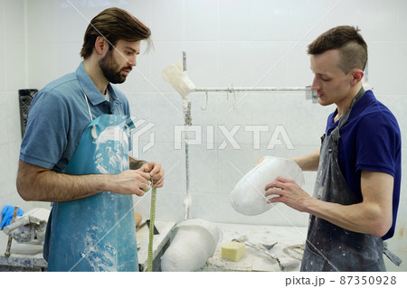 Young man in apron showing coworker prosthetic socket Young man in apron showing coworker prosthetic socket 87350928
