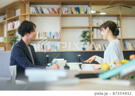 オフィス内で本を読み勉強会をする若い男女 87354932