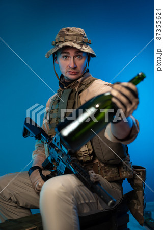 a drunk army soldier in military clothes with a bottle of alcohol in his hand offers to drink 87355624