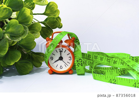 Measure tap with orange clock on white wooden background. Diet concept. Measure tap with orange clock on white wooden background. Diet concept. 87356018