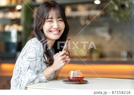 カフェで紅茶を飲みながらスマホを見ている若い女性 87358216