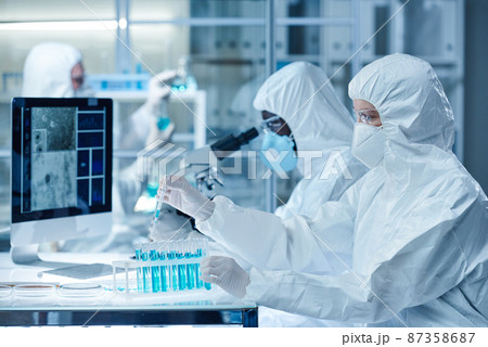 Group of scientist in protective wear examining the samples of dangerous virus in test tubes with microscope in laboratory 87358687